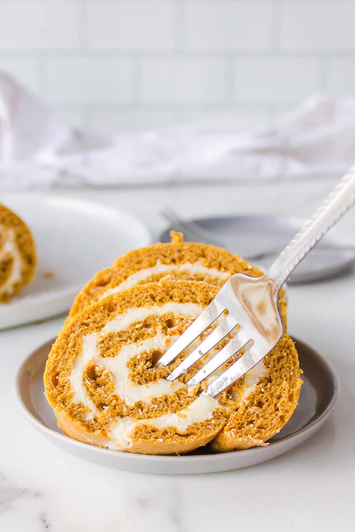 fork in cake mix pumpkin roll with cream cheese frosting served on a taupe plate