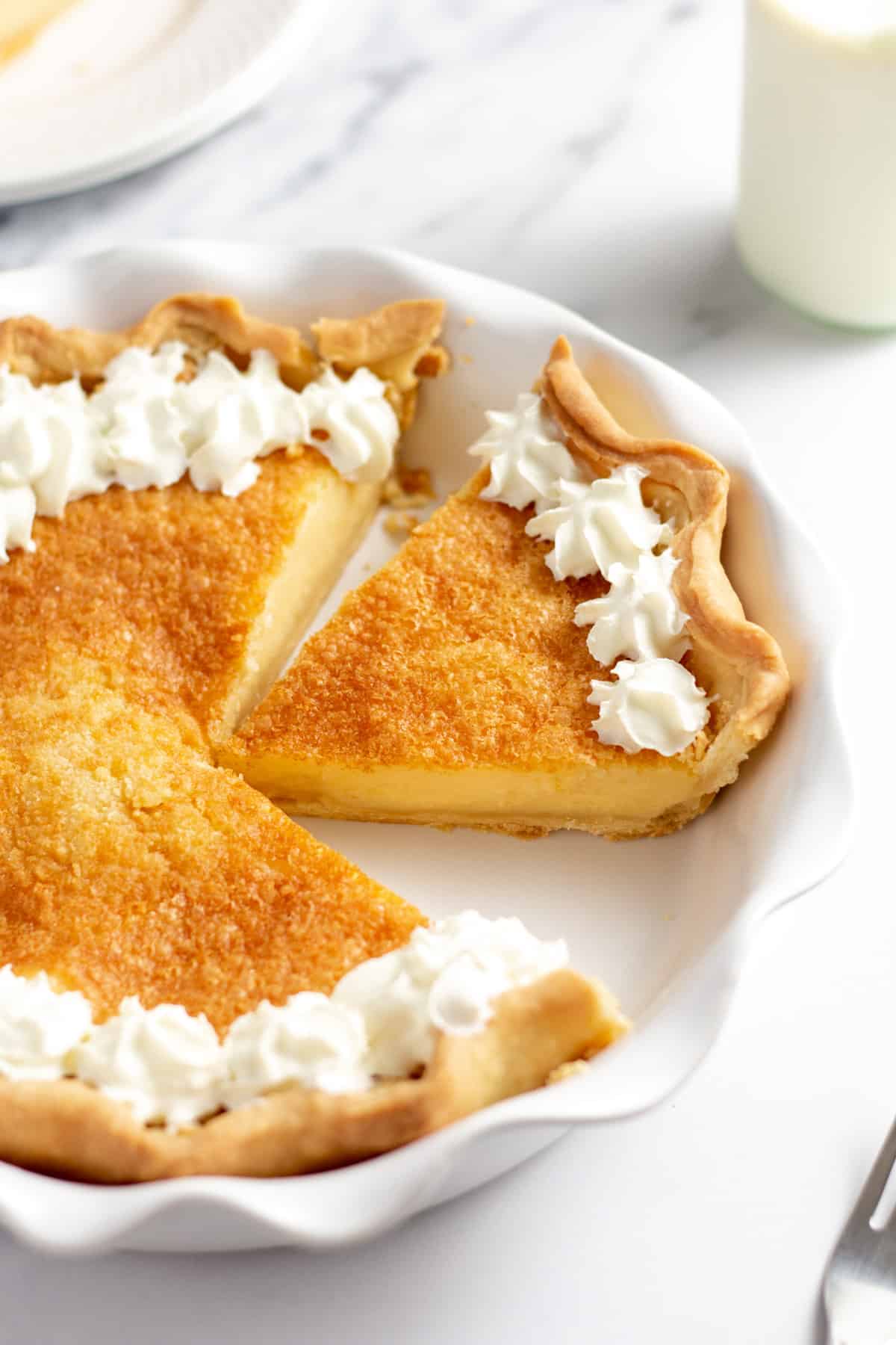 baked buttermilk pie in a white dish, with a slice cut
