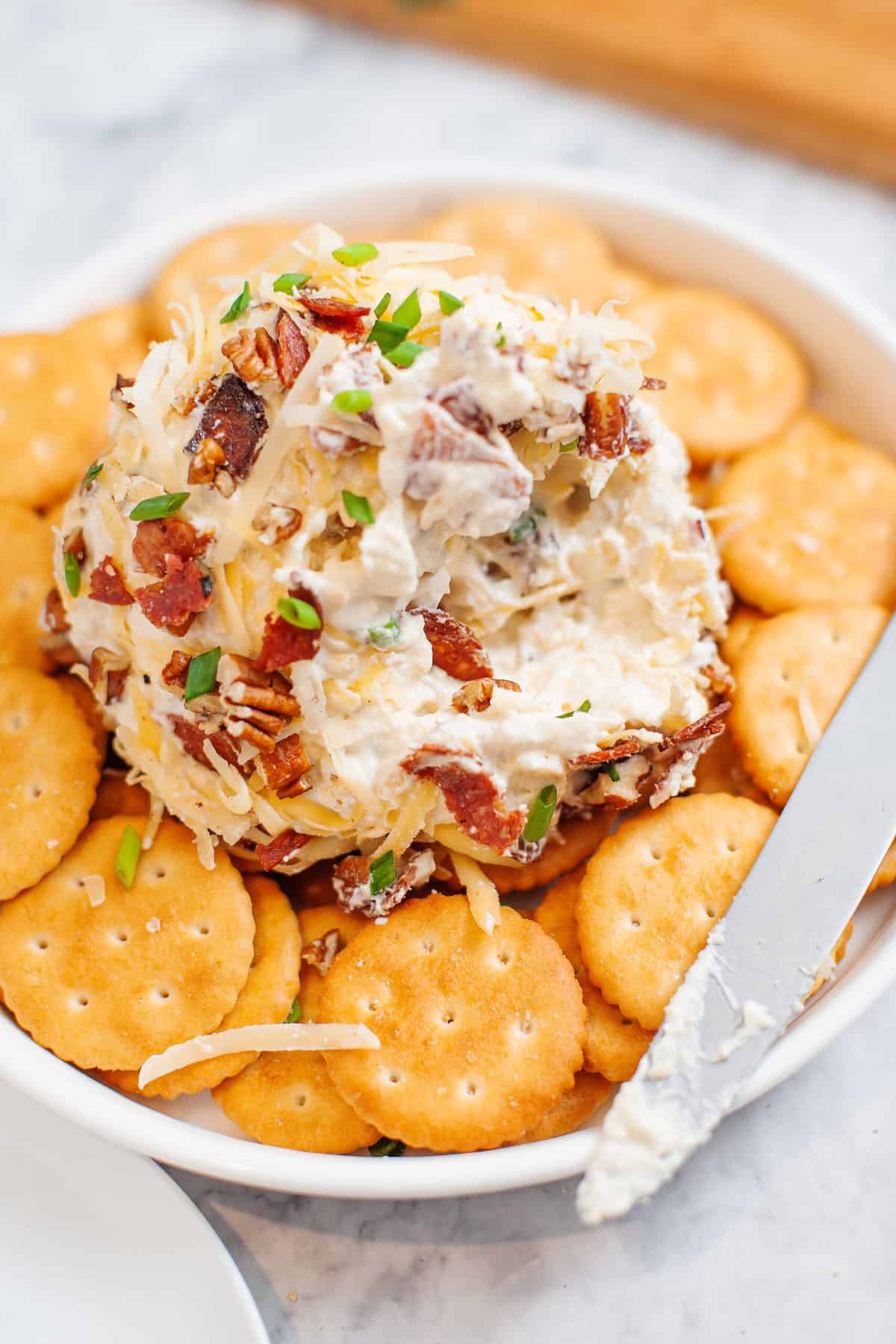 cheese ball sitting on top of a bed of rtiz crackers served in a white shallow bowl