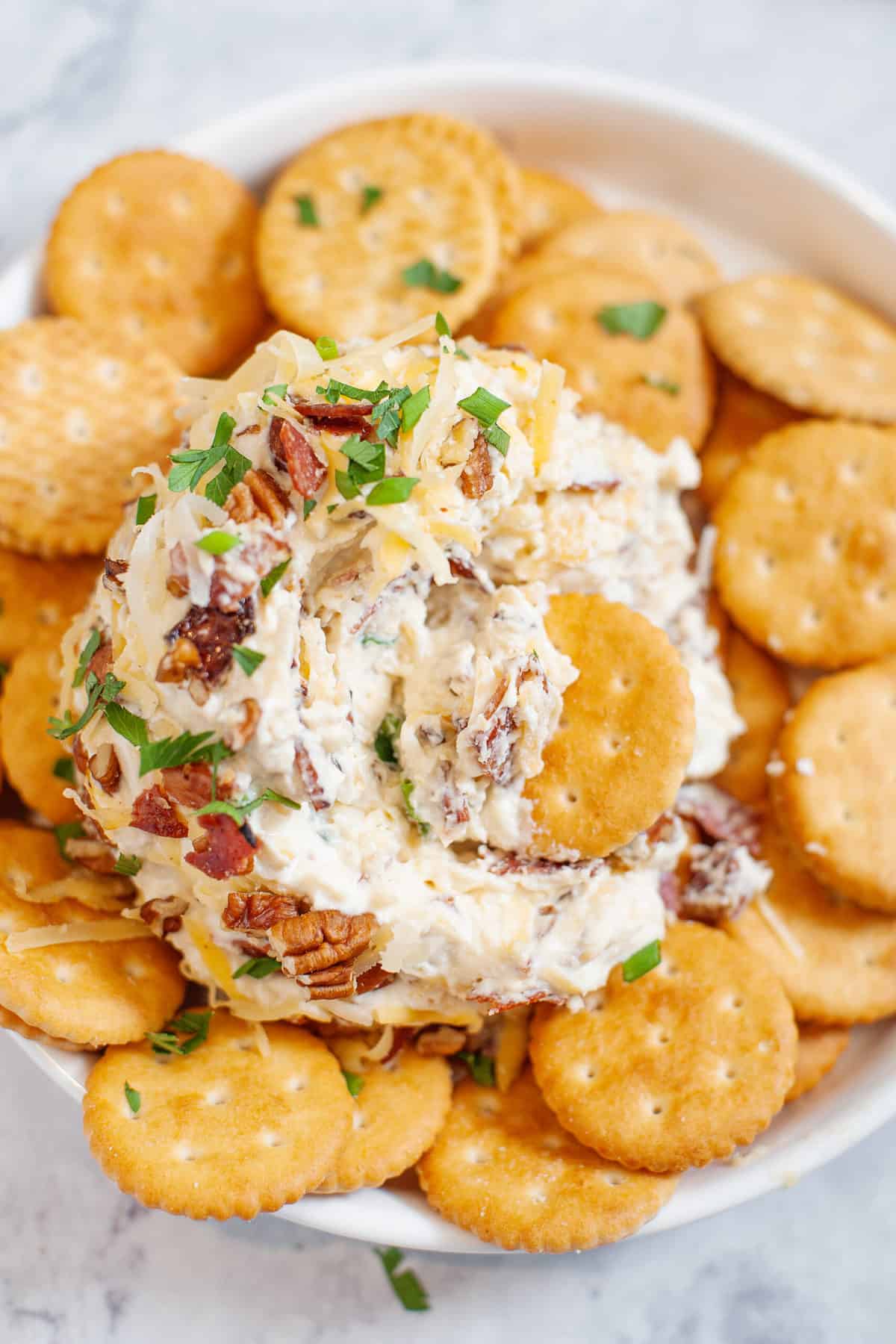 cheese ball sitting on top of a bed of ritz crackers served in a white shallow bowl