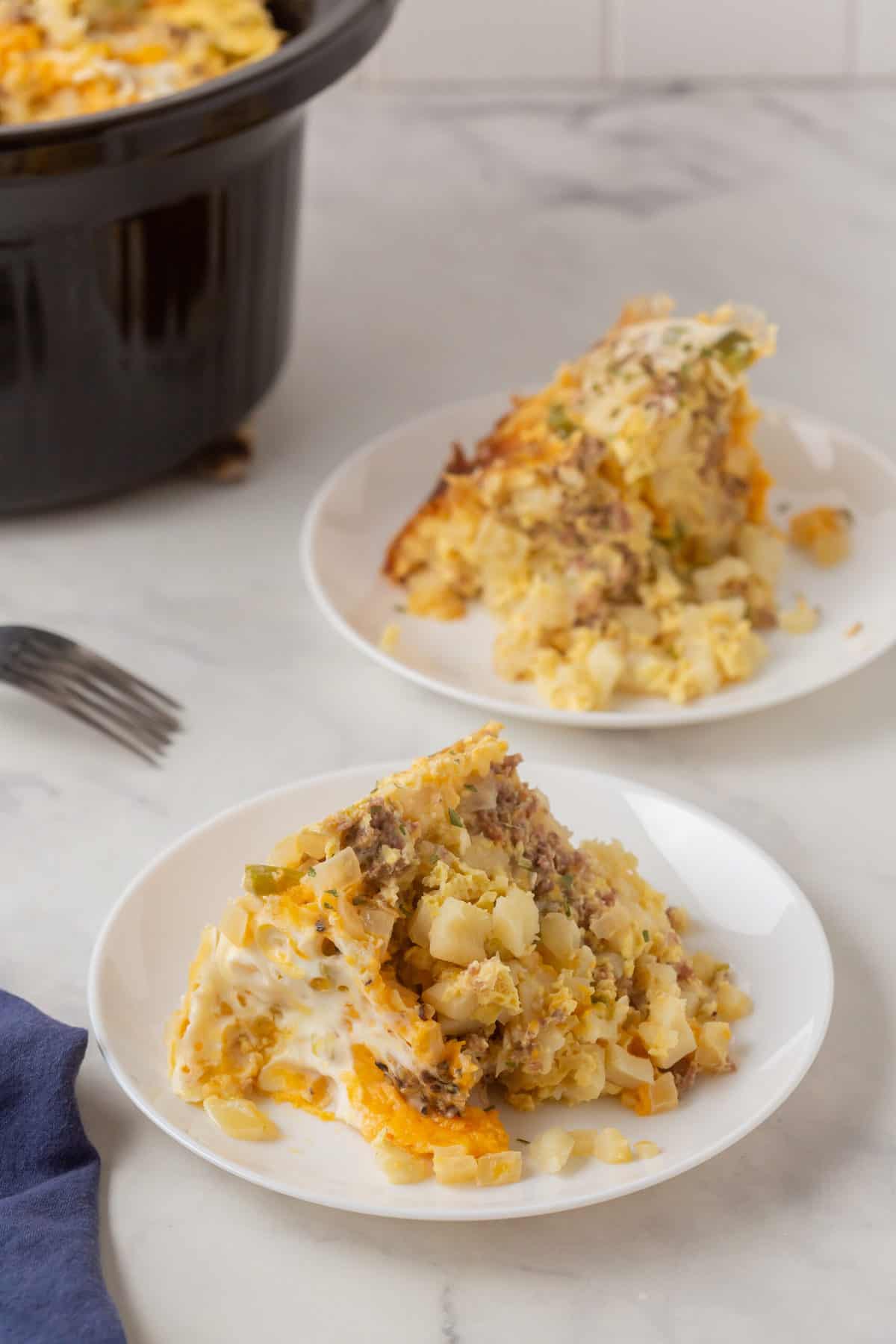 serving of crockpot breakfast casserole on a white plate one in the foreground and one in the background
