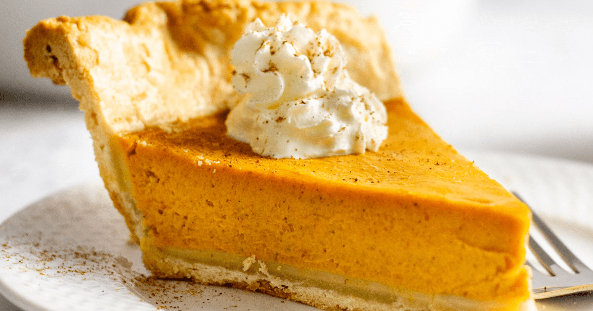 slice of homemade pumpkin pie with whipped cream served on a white plate