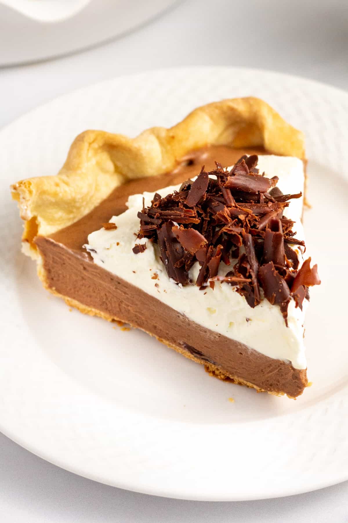slice of french silk pie with homemade pie crust whipped cream and chocolate shavings served on a white plate