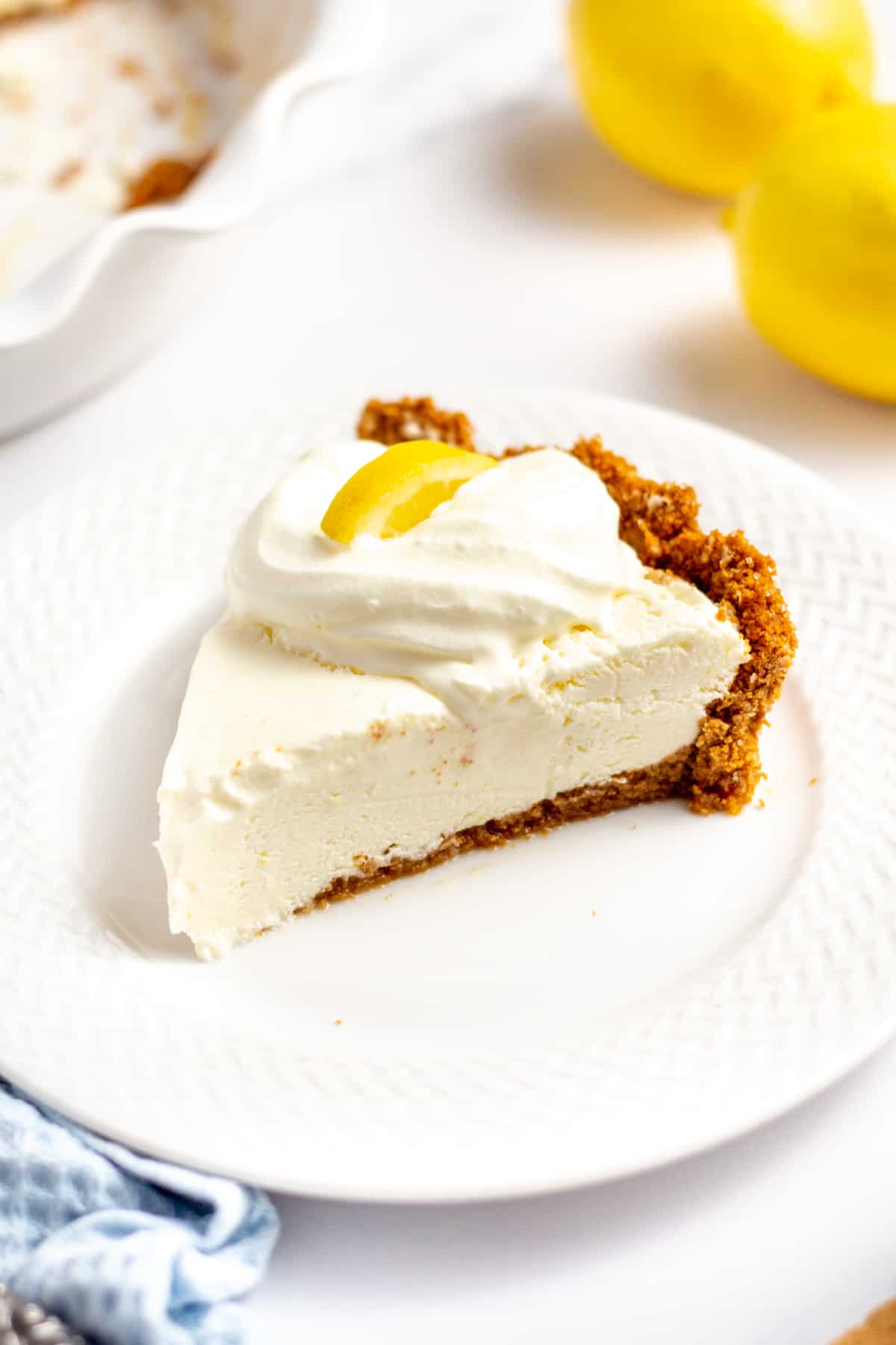 slice of lemon cream pie with graham cracker crust and a dollop of cool whip with a slice of lemon