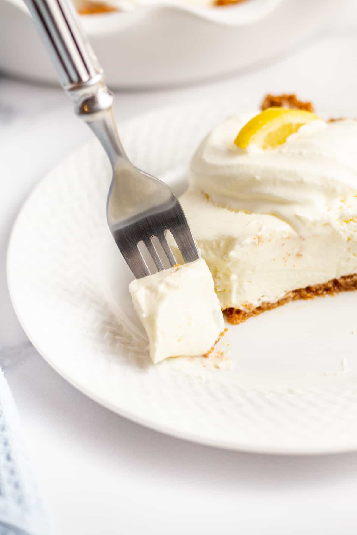 slice of lemon cream pie on a white plate with a forkful of pie