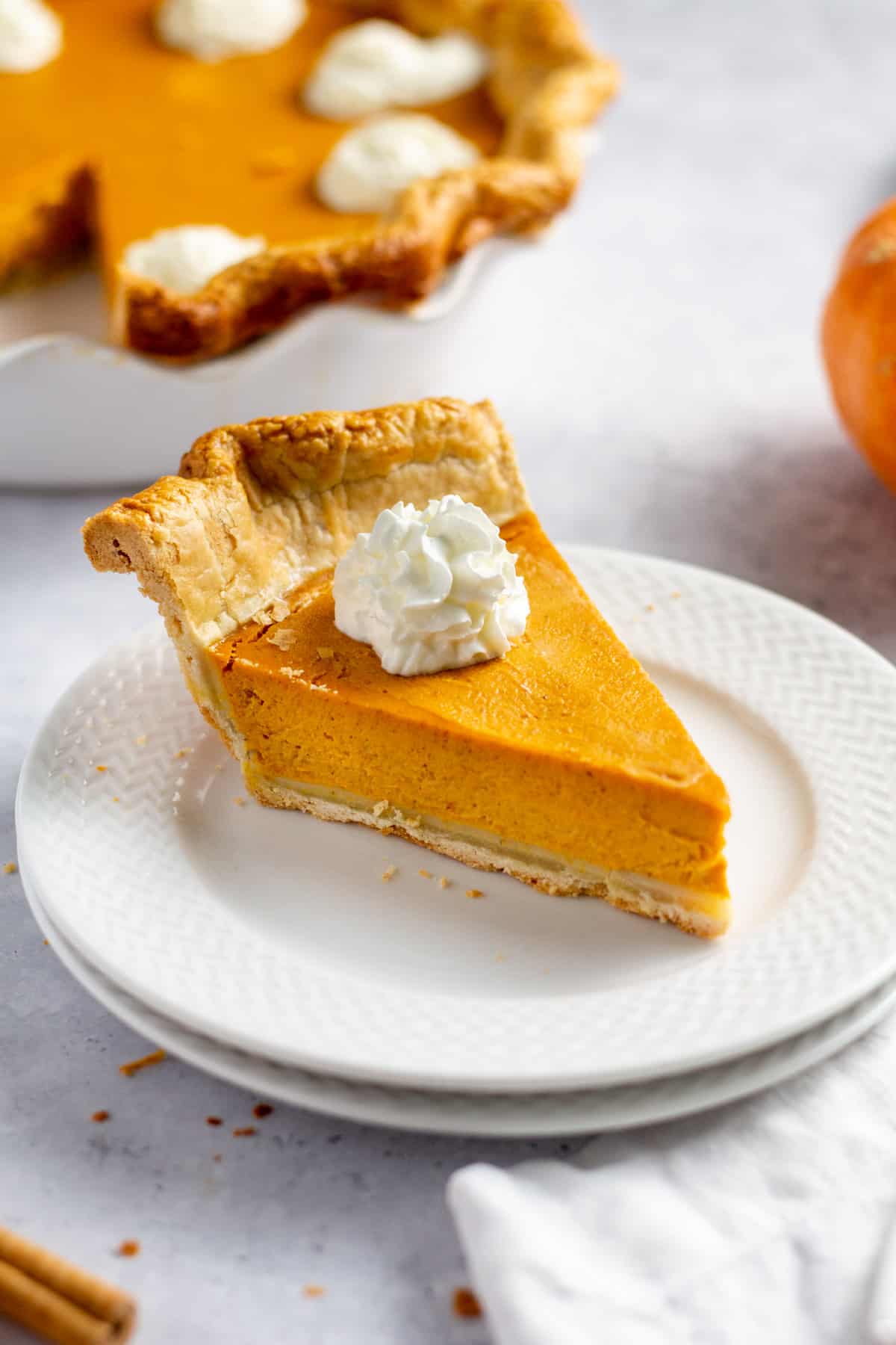 slice of pumpkin pie with homemade crust topped with whipped cream served on a white plate