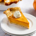 slice of pumpkin pie with whipped cream served on a white plate