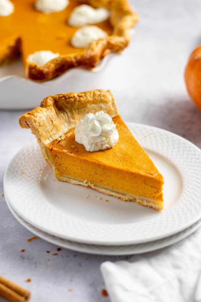 slice of pumpkin pie with whipped cream served on a white plate
