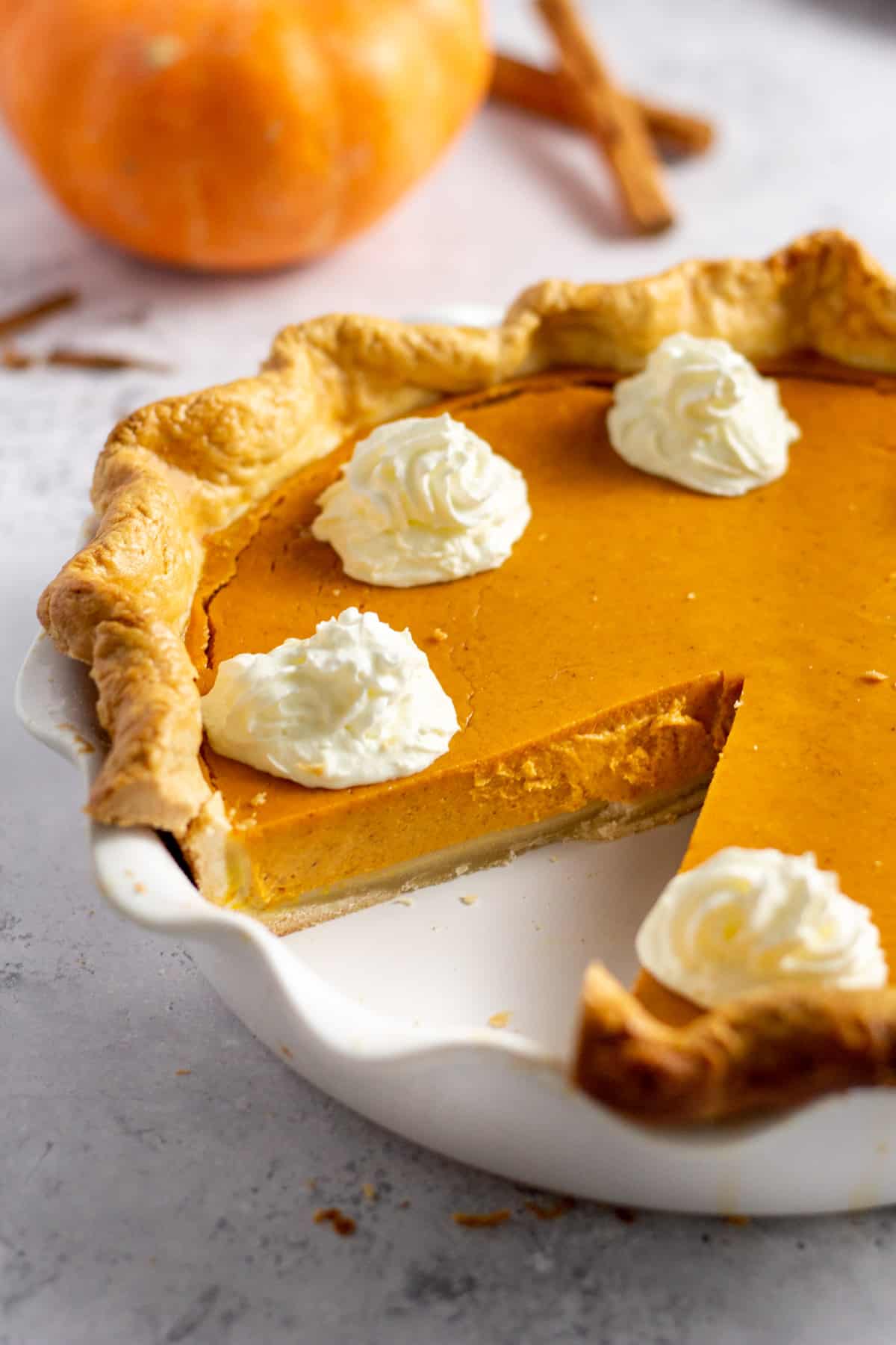 homemade pumpkin pie with homemade crust served in a ceramic pie dish with a whipped cream design and a slice taken out of the pie