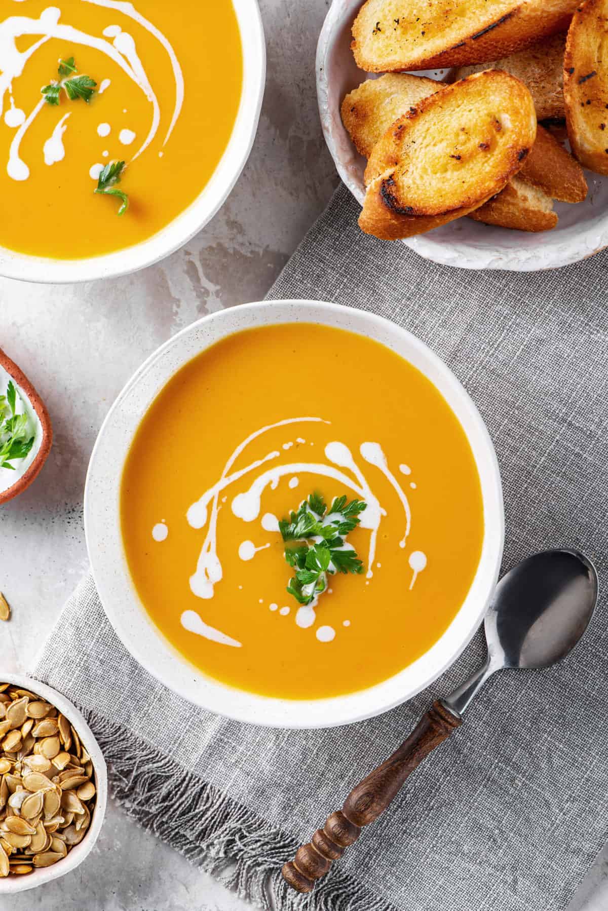 butternut squash soup with a sour cream swirl design and cilantro served in a white bowl and a silver spoon sitting next to the bowl