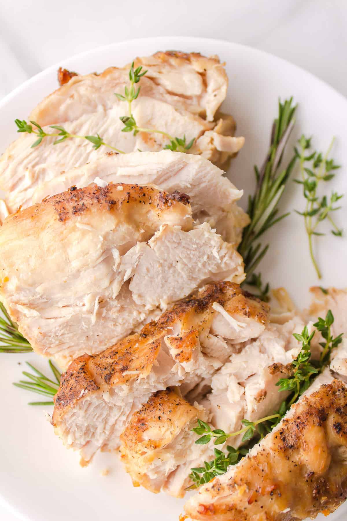 slice crockpot turkey breast served on a white plate with homemade gravy and rosemary