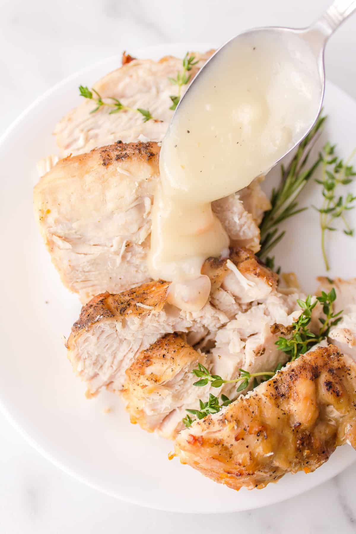 slice turkey breast made from a slow cooker served on a white plate with homemade gravy and rosemary
