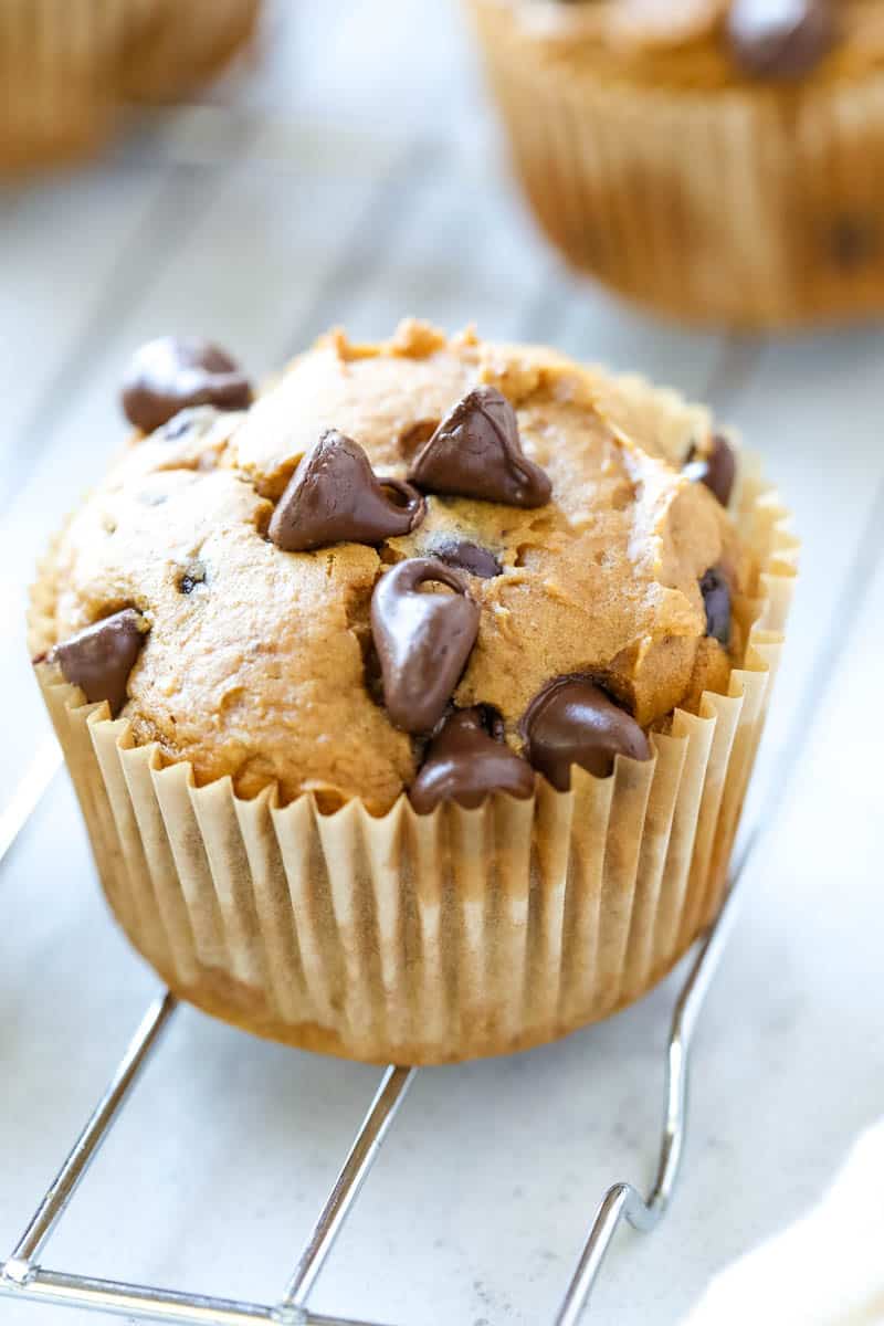 Pumpkin chocolate chip muffin on a table in a brown wrapper. 