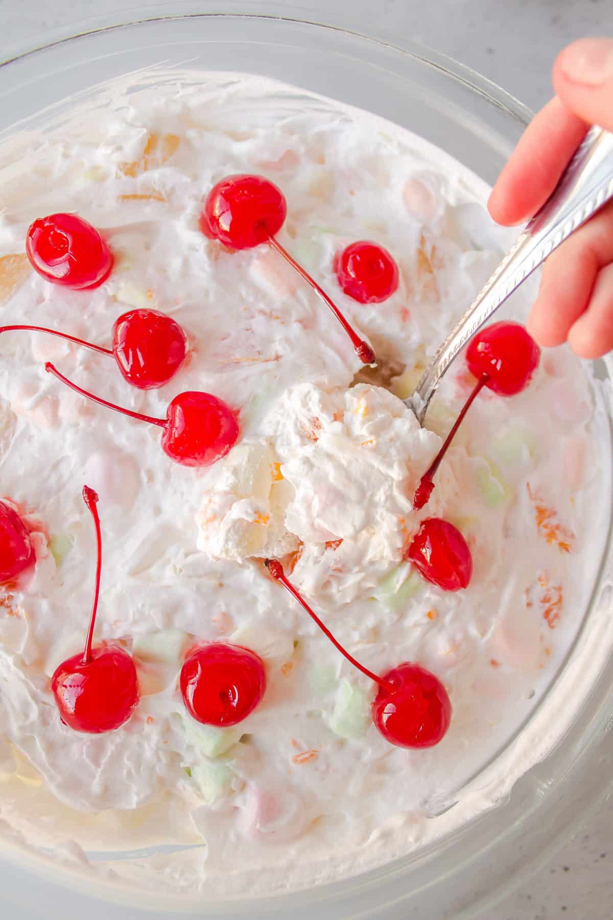 ambrosia salad with cherries on top served in a white glass bowl