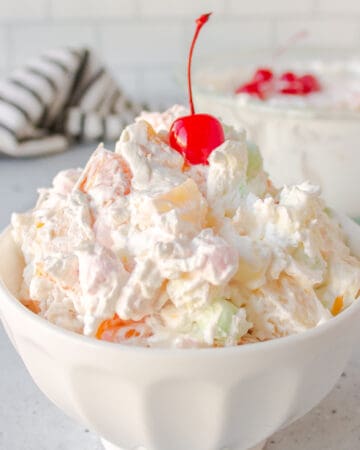 ambrosia salad with a cherry on top served in a white bowl