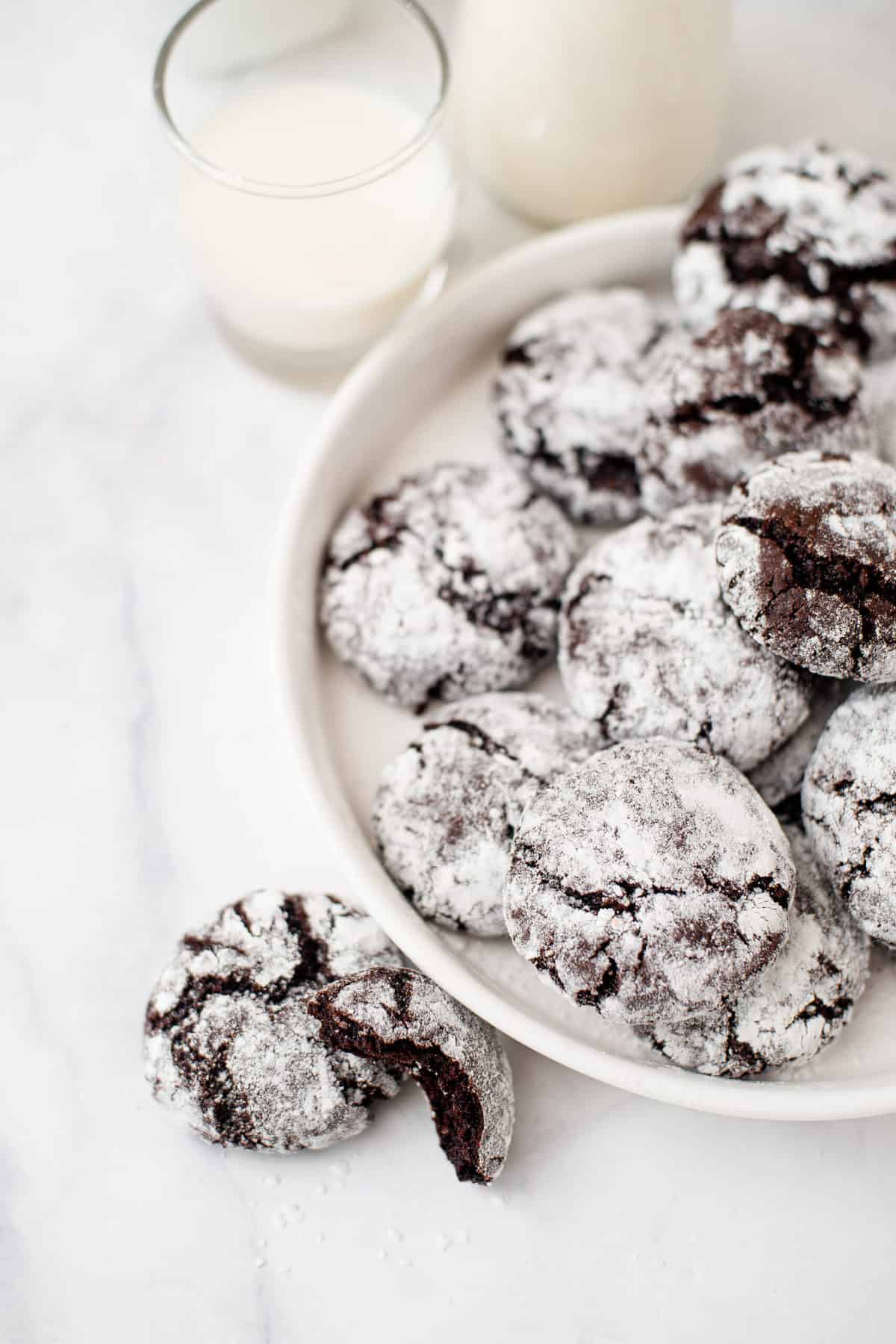 chocolate crinkles served on a white round plate with two cookies sitting next to the plate on a marble countertop
