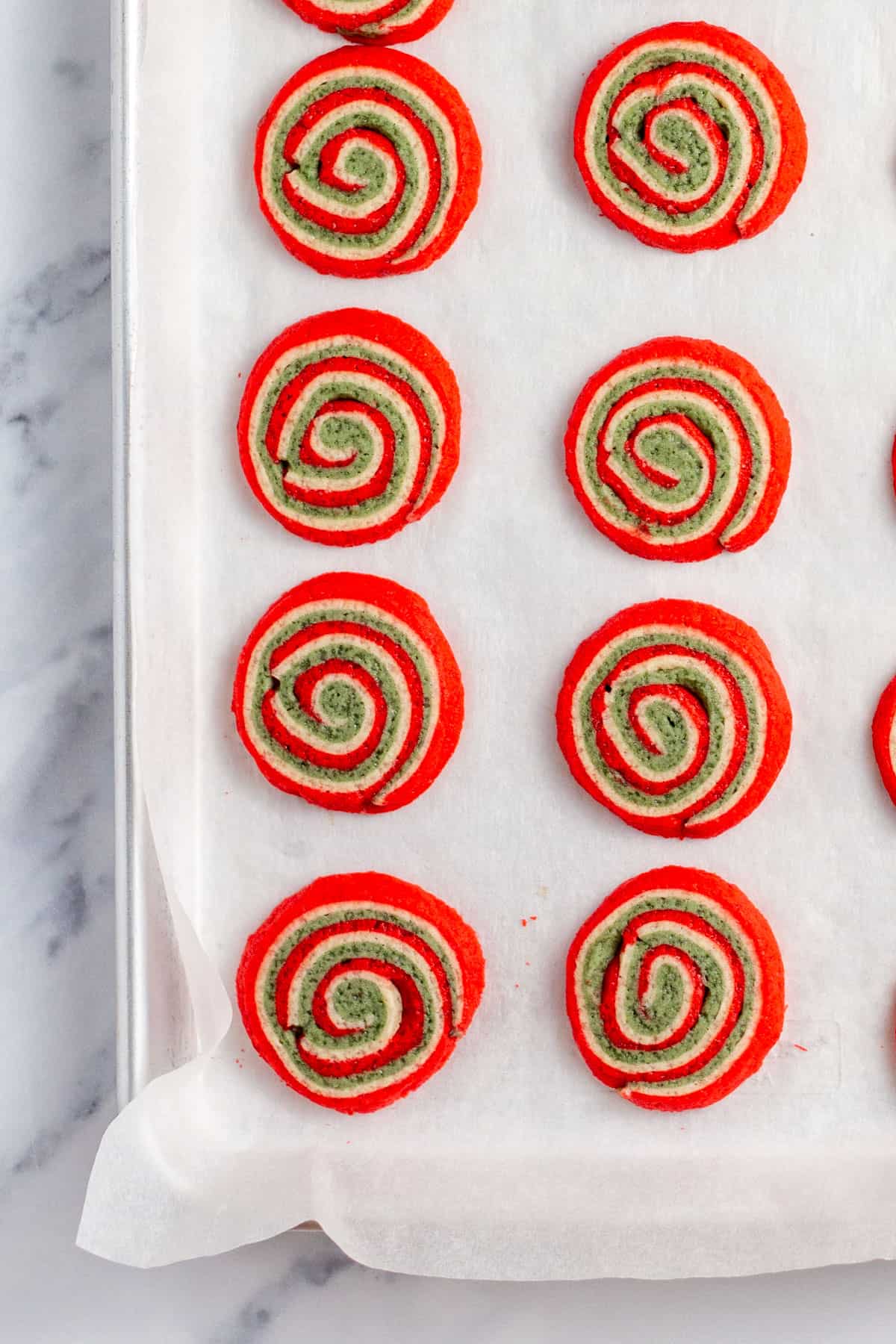 red white and green christmas pinwheel cookies on a baking sheet with parchment paper