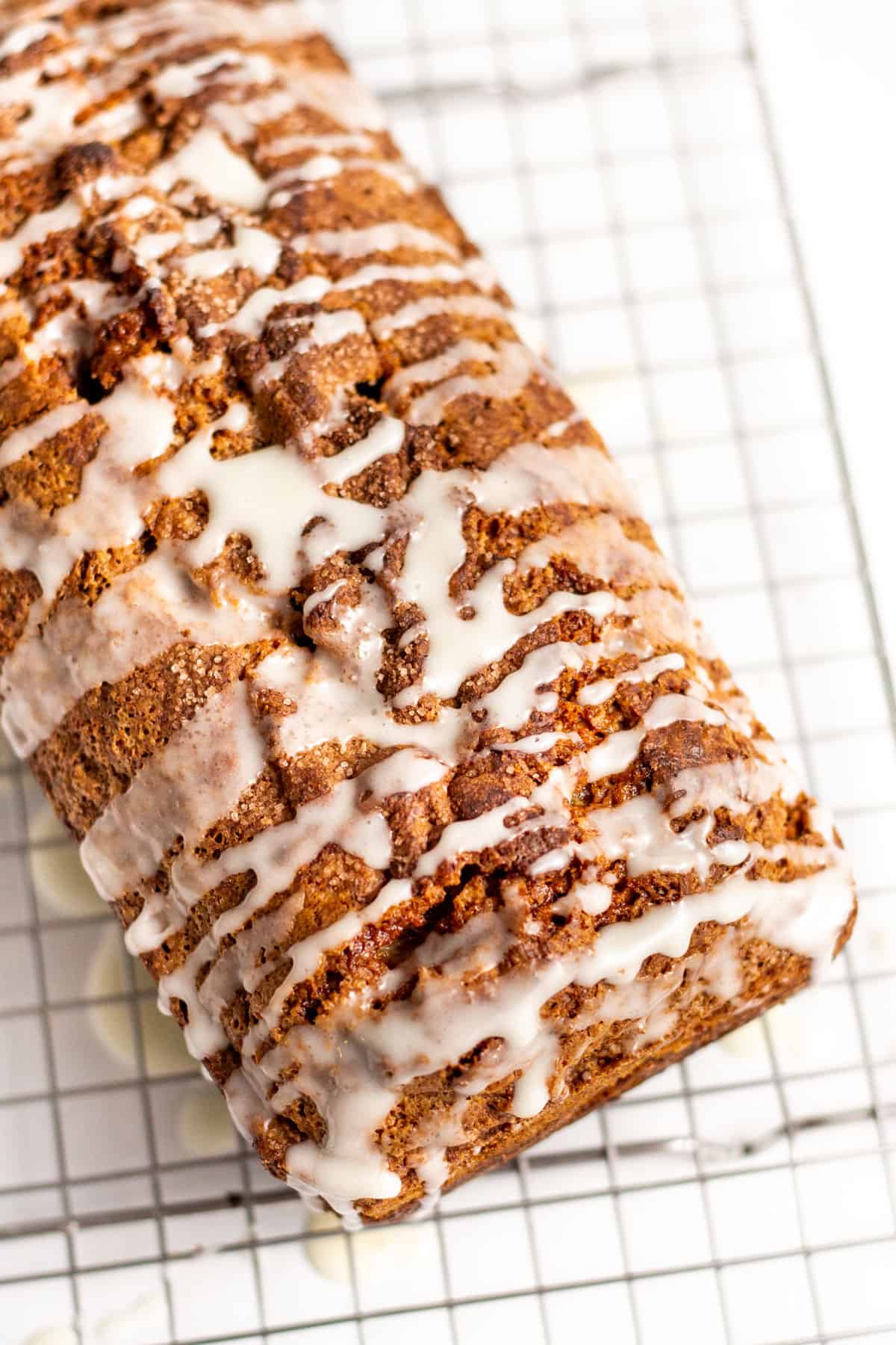 cinnamon swirl bread loaf with a cream glaze on top sitting on a wire cooling rack