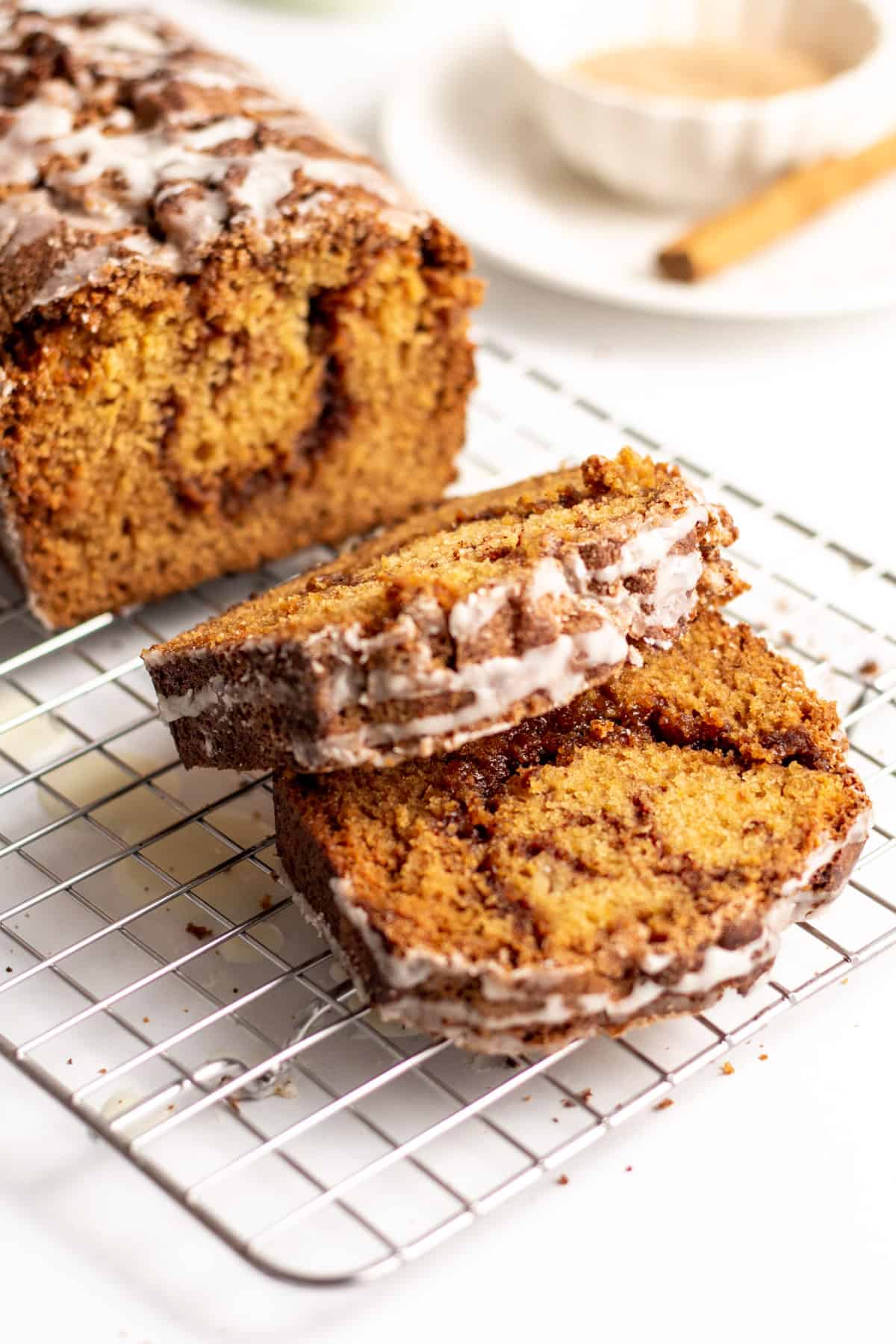 sliced cinnamon swirl bread loaf with a cream glaze frosting sitting on a wire cooling rack
