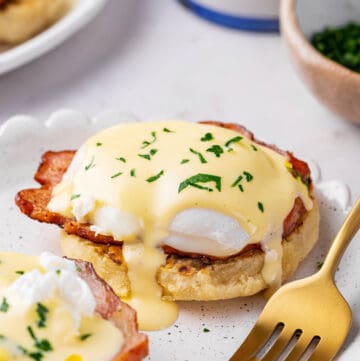 eggs benedict with homemade hollandaise sauce and ham served on a plate with a gold fork