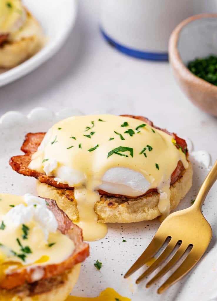 eggs benedict with homemade hollandaise sauce and ham served on a plate with a gold fork