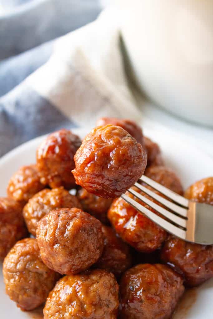 Meatballs covered in sauce in a bowl with a fork in one of them.