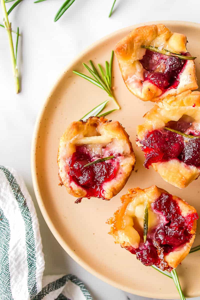 cranberry brie bite garnished with rosemary served on a light orange plate