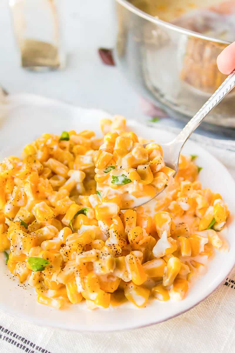 homemade creamed corn in a white dish on a spoon