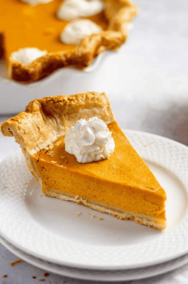 slice of homemade pumpkin pie with a dollop of whipped cream served on a white plate