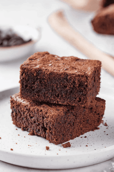 two square slices of homemade brownies stacked sitting on a speckled round plate