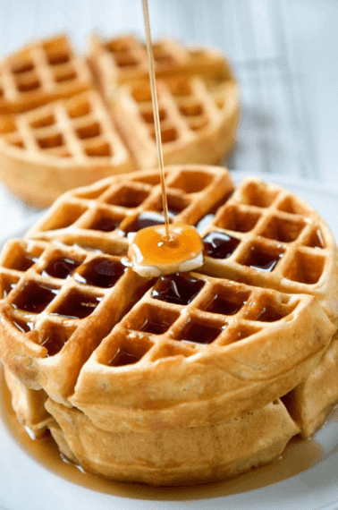 stack of homemade waffles with a slab of butter on top and maple syrup pouring over it