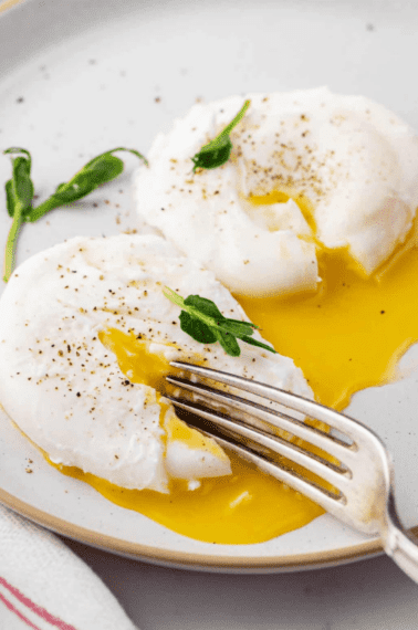 fork cutting poached eggs served on a plate