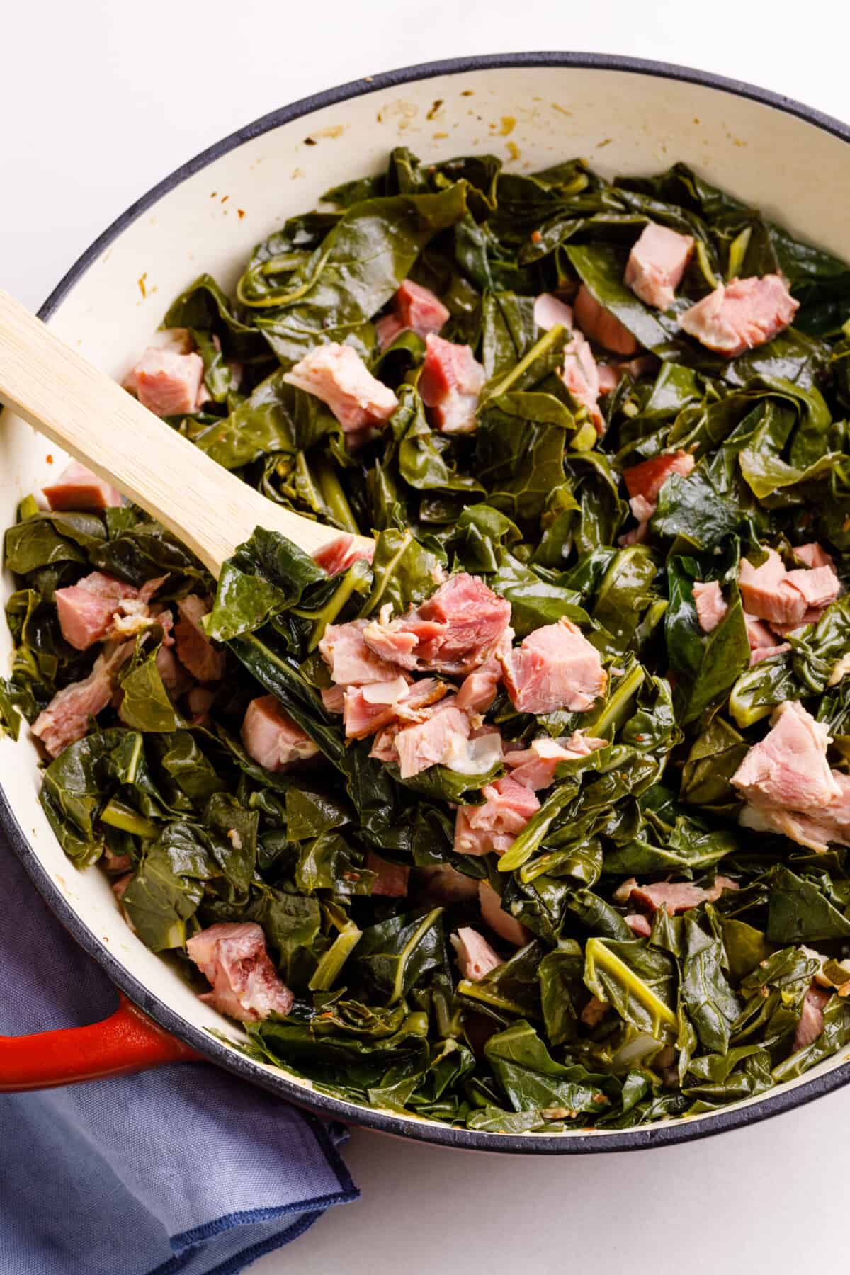 Collard greens with ham hocks and bacon being served on a wooden spoon.