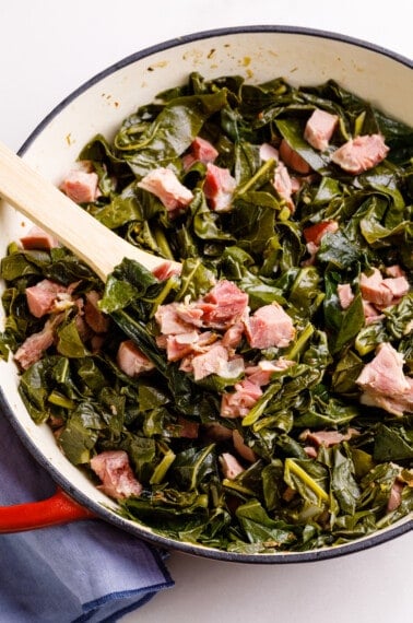 Collard greens with ham hocks and bacon being served on a wooden spoon.