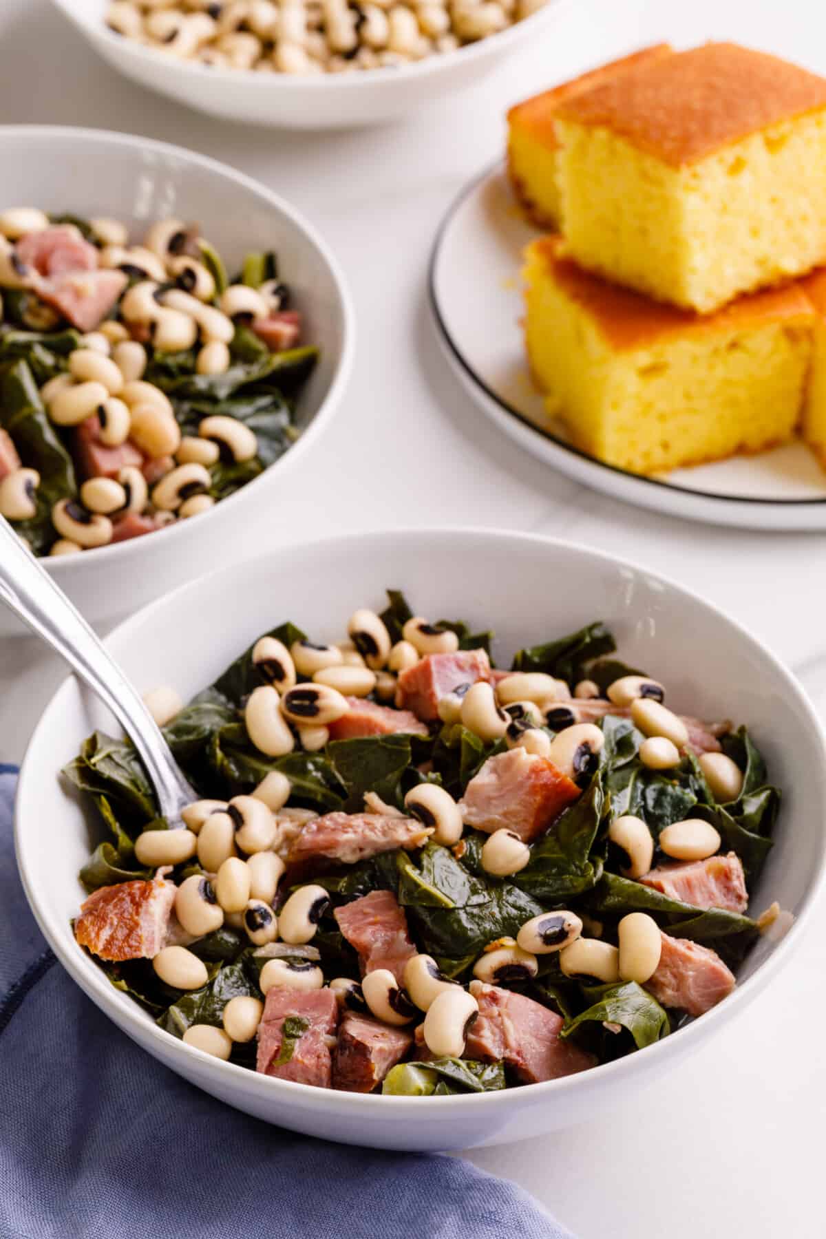 Bowls of collard greens next to a plate of cornbread.