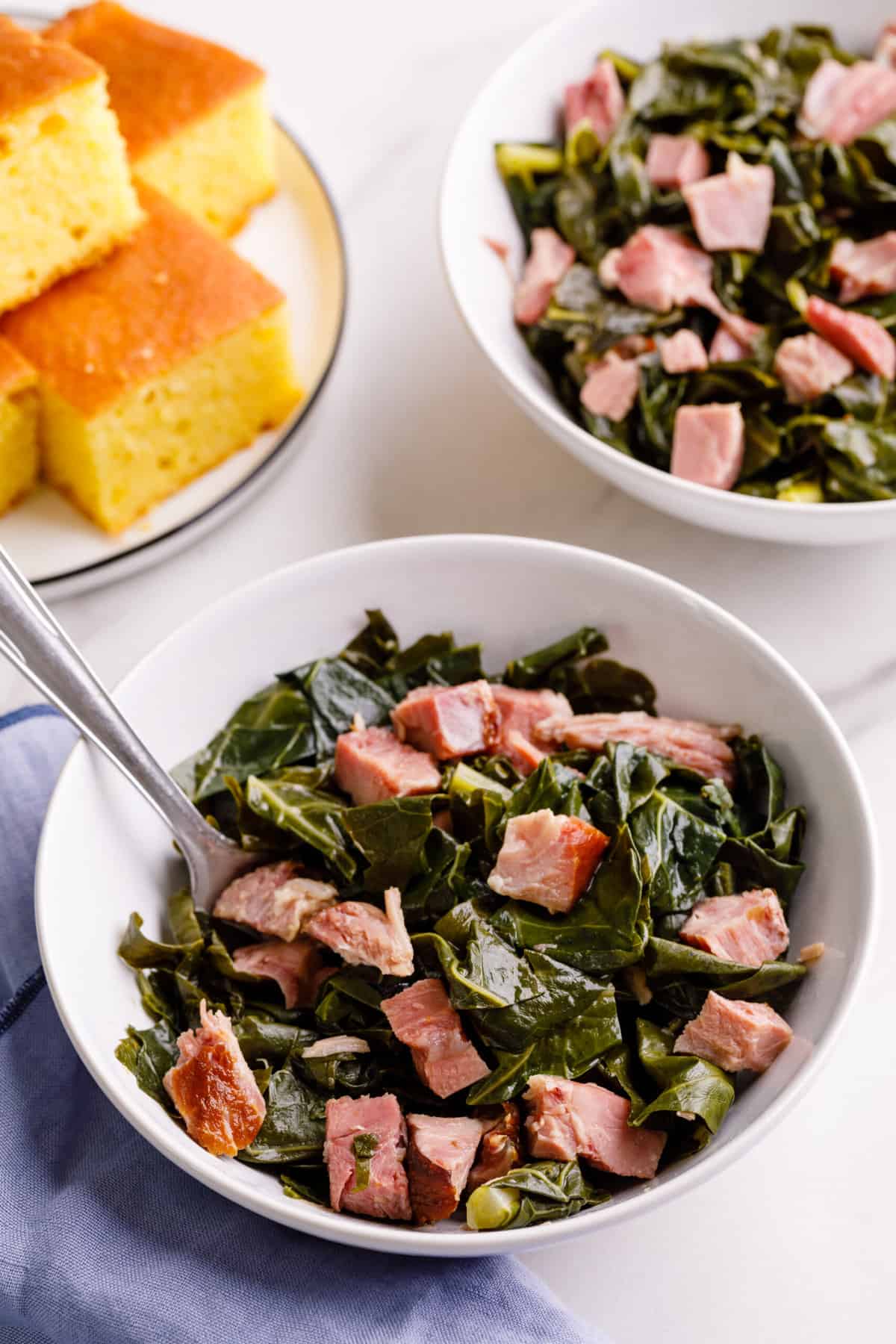 serving of collard greens with ham served in a white round bowl with a silver spoon