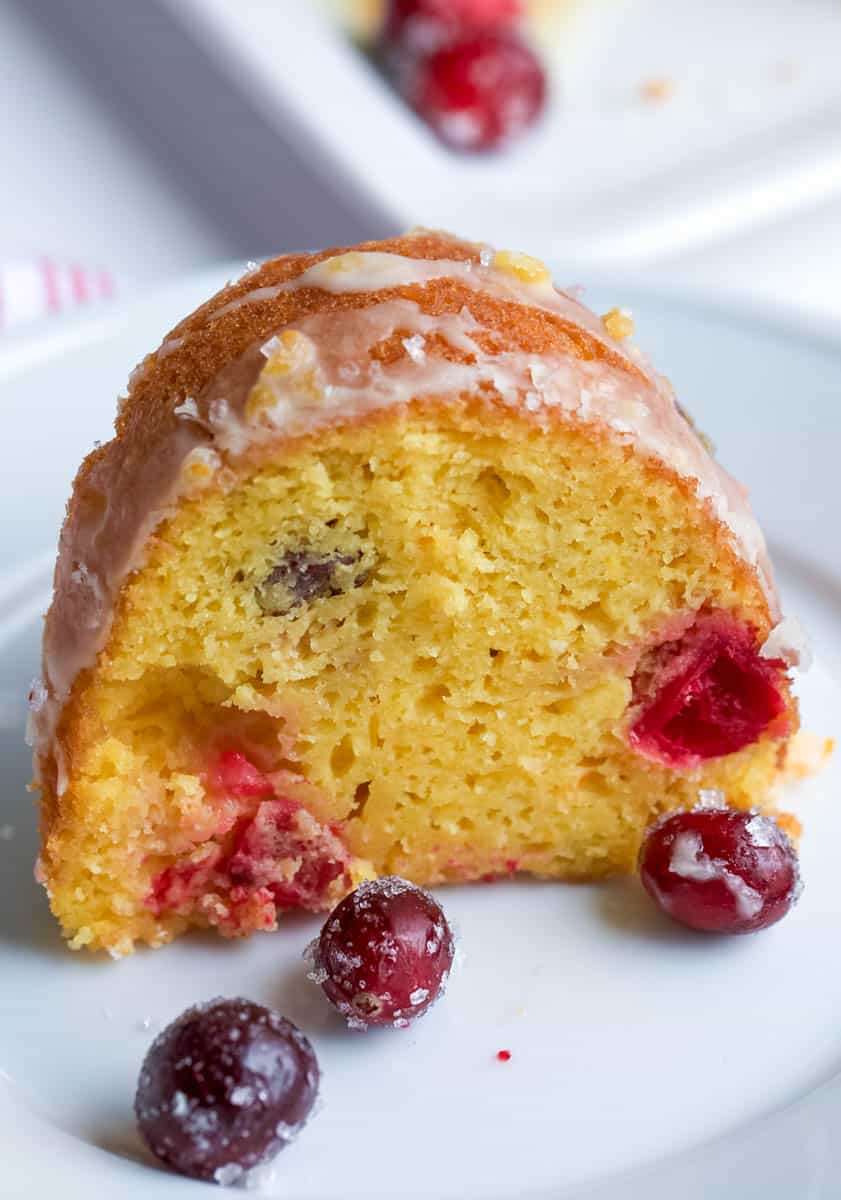 piece of orange bundt cake on white plate with sugared cranberries
