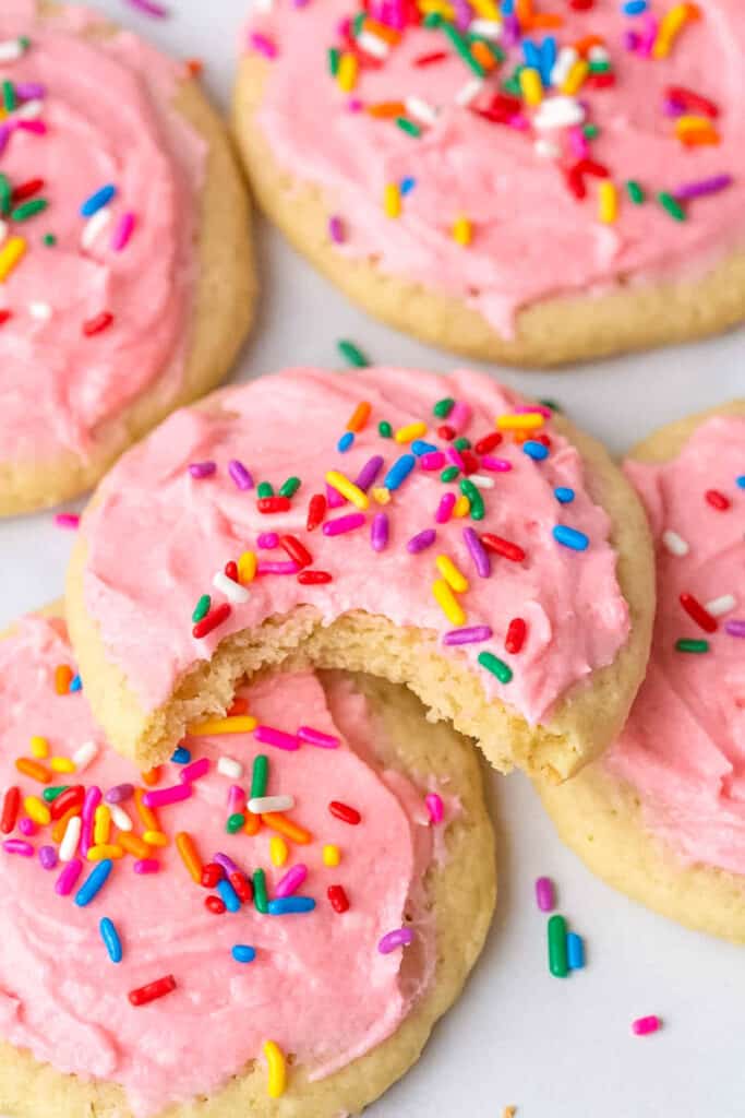 a bite taken out of a pink frosted sugar cookie with rainbow sprinkles