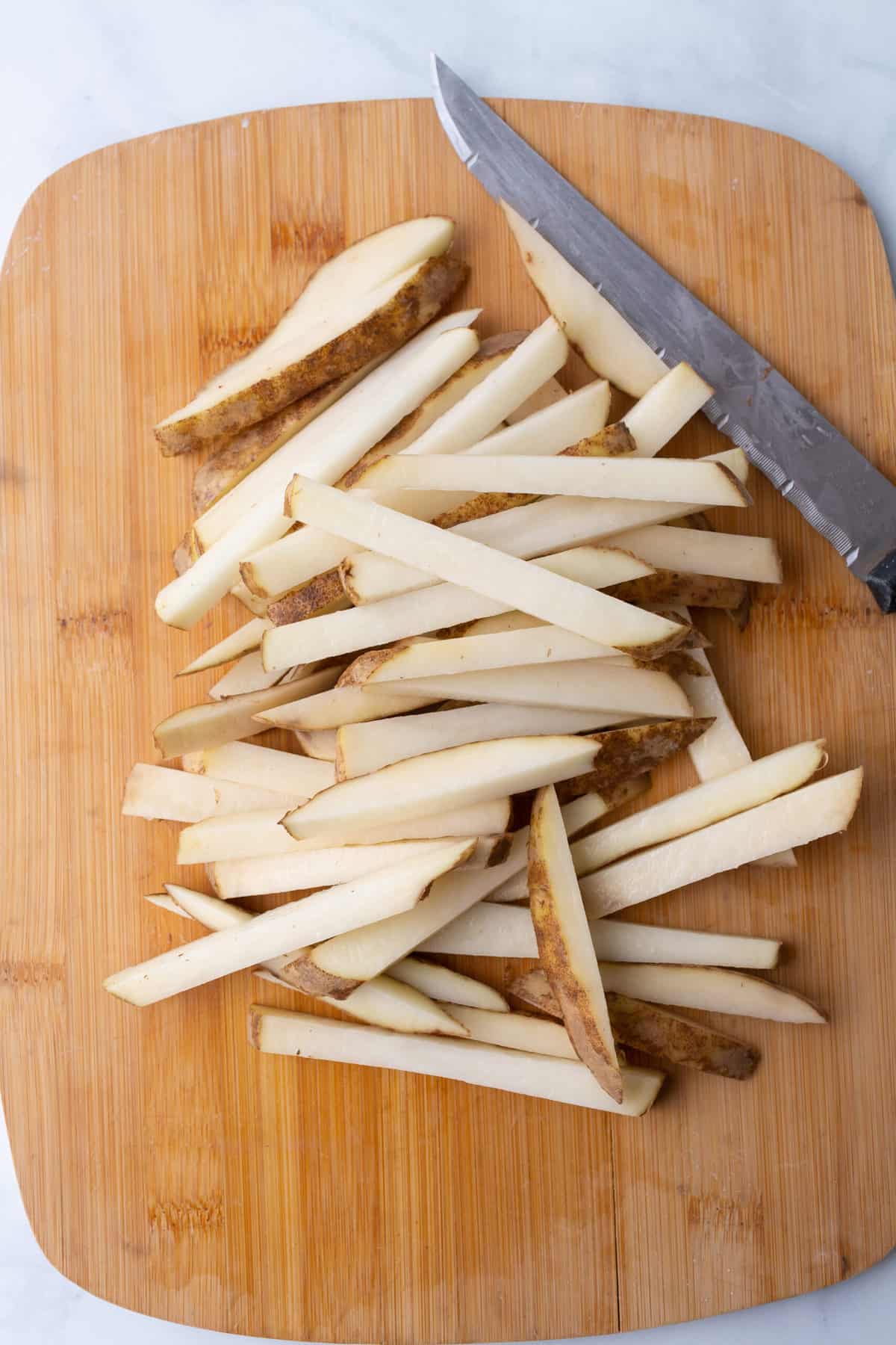 Top image of russet potatoes, cut into french fries when cutting board.