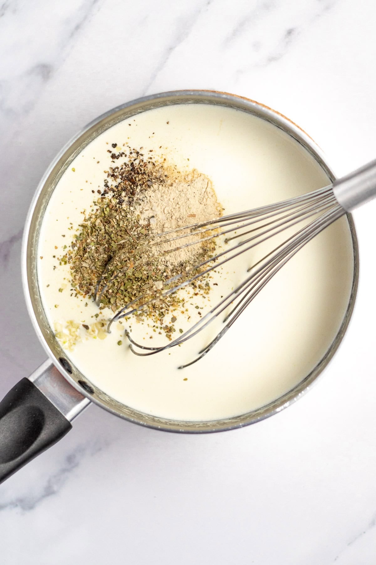 Whisking seasonings into chicken alfredo sauce with cream cheese.