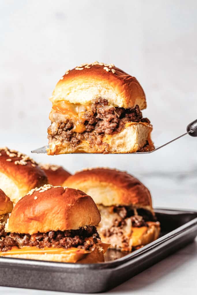 cheeseburger sliders on a baking sheet and a slider on a spatula