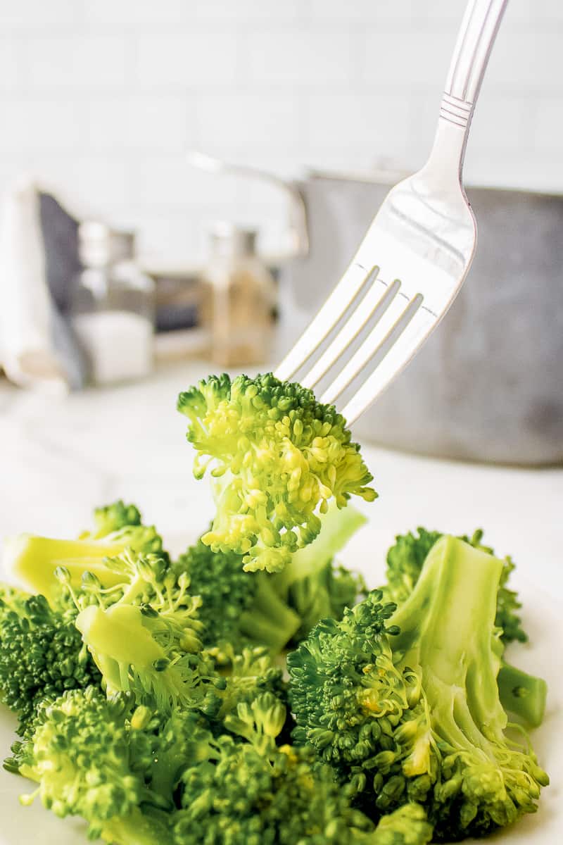 steamed broccoli on a silver fork served on a white plate