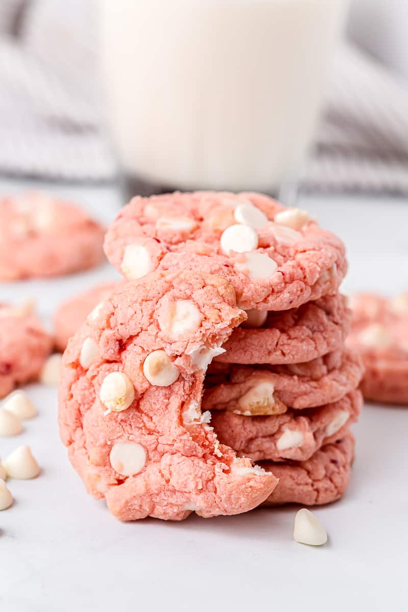 stack of strawberry cake mix cookies with one of the cookies having a bite taken out of it