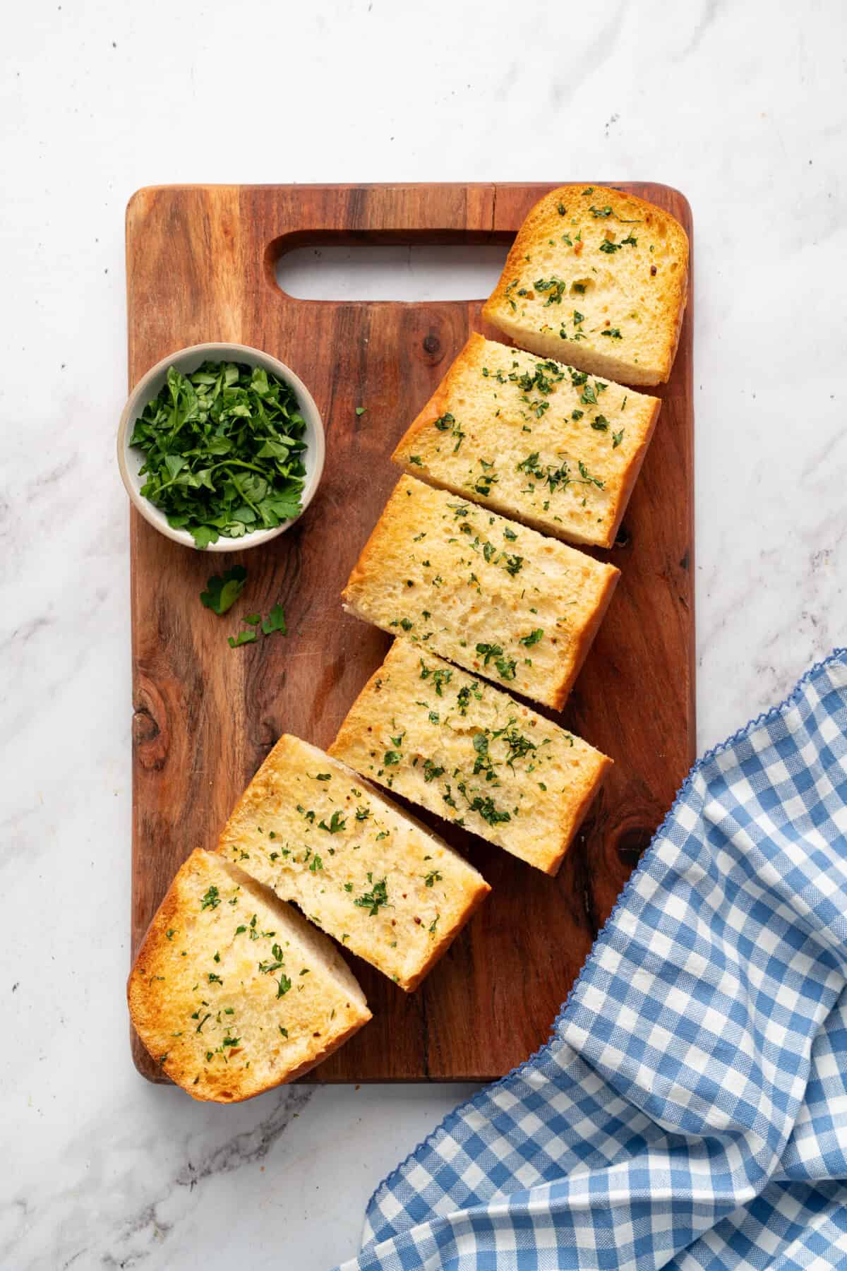 Homemade garlic bread sliced on wooden board.