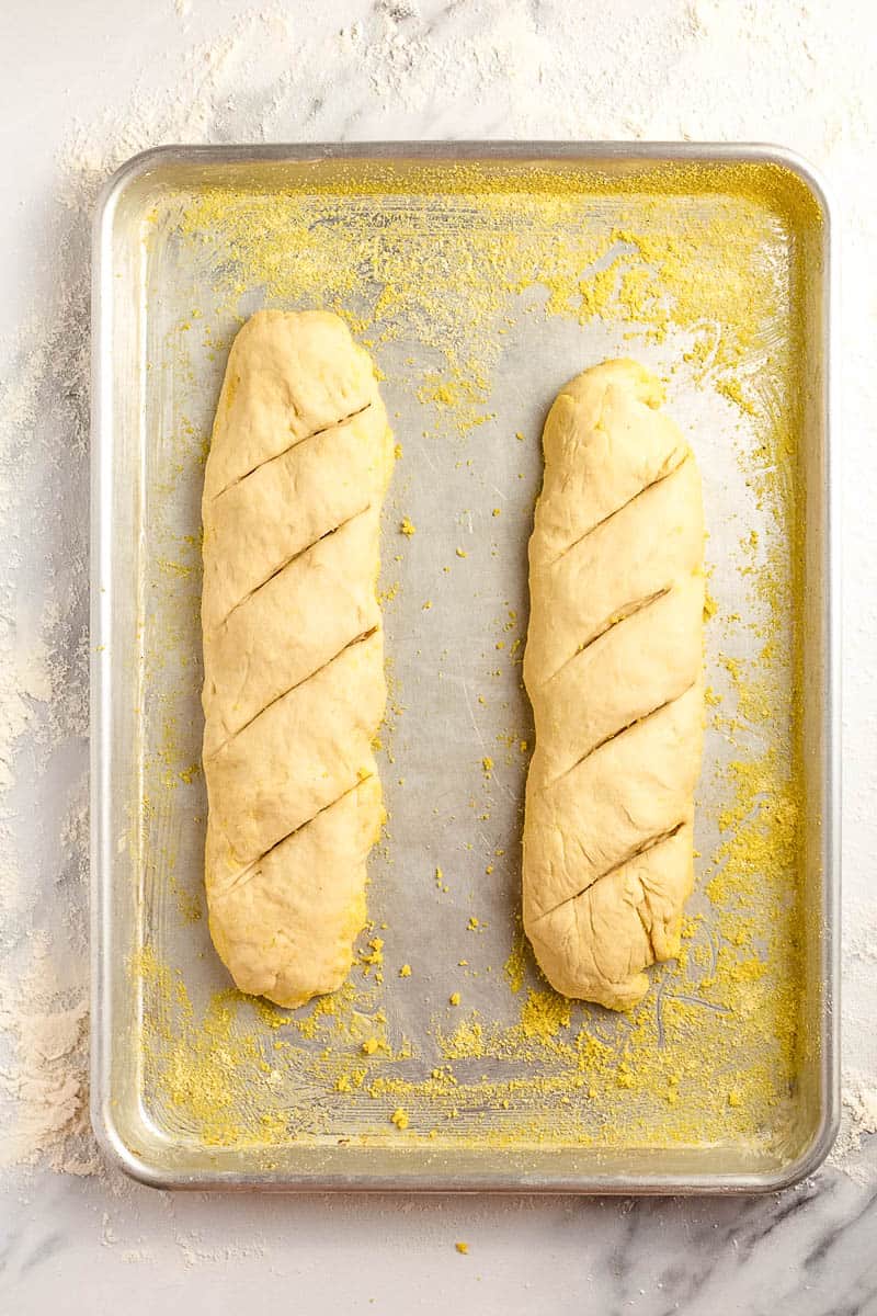 two french bread dough loaves scored and sitting on a baking sheet.