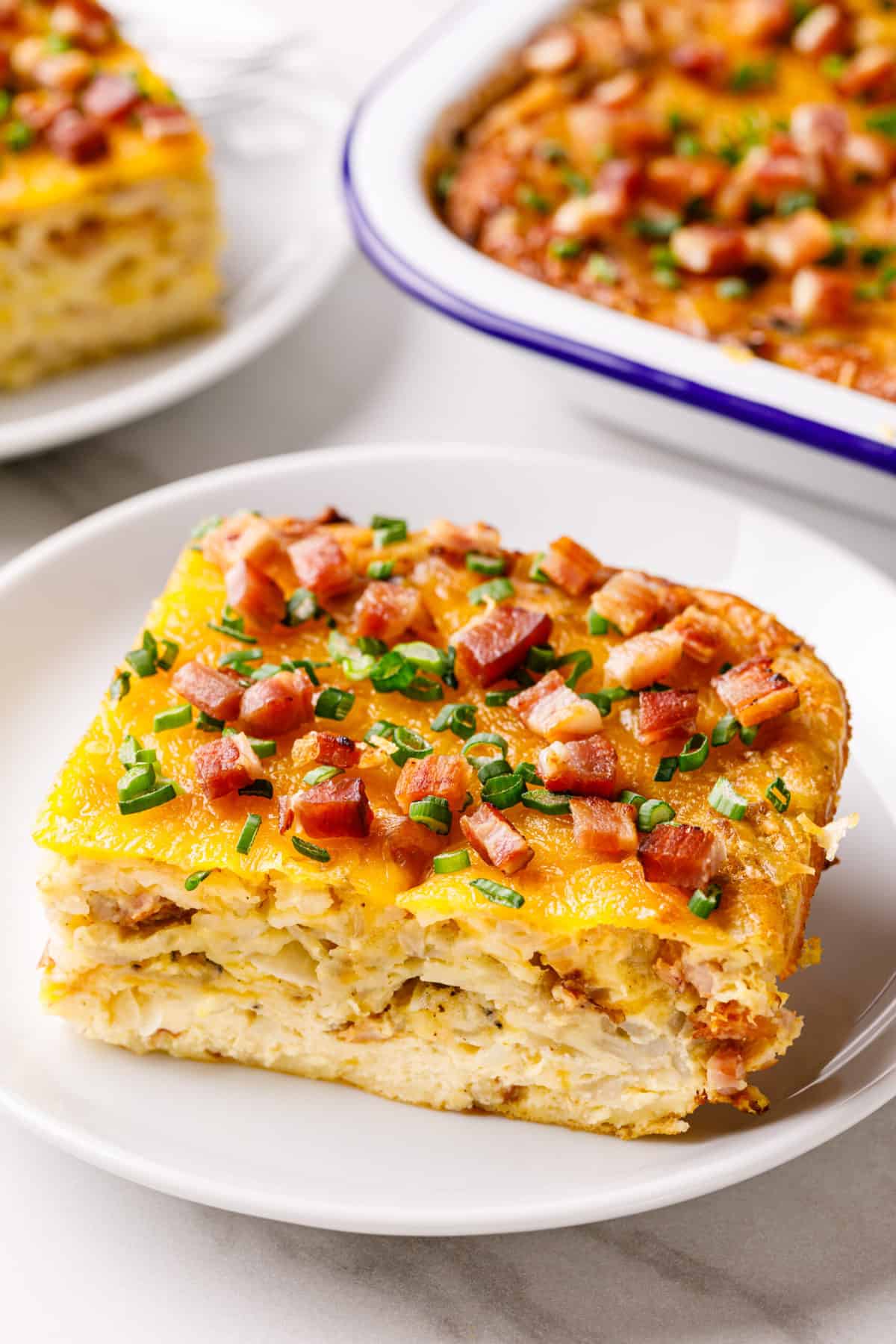 square serving of bisquick breakfast casserole topped with bacon and green onions served on a white round plate