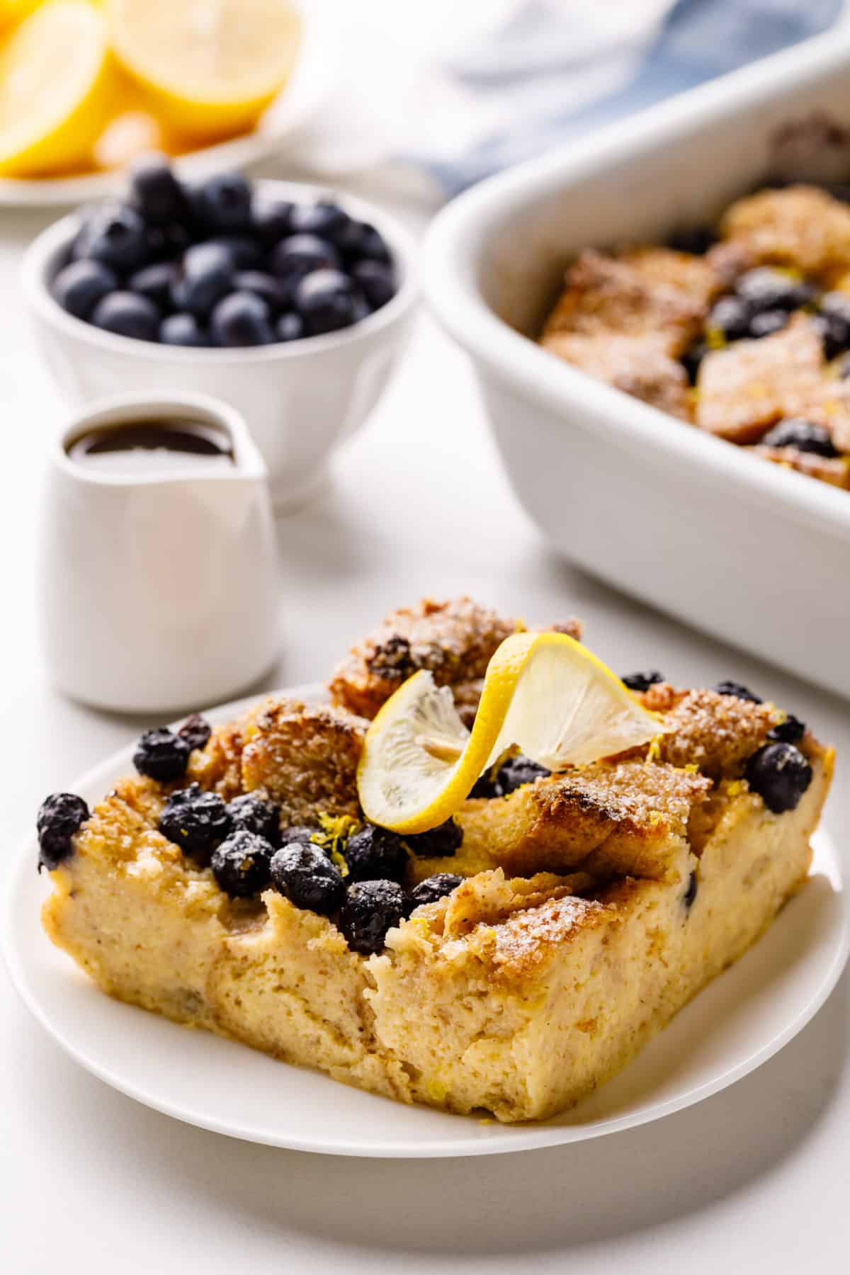 square slice serving of blueberry french toast casserole topped with a lemon slice and blueberries