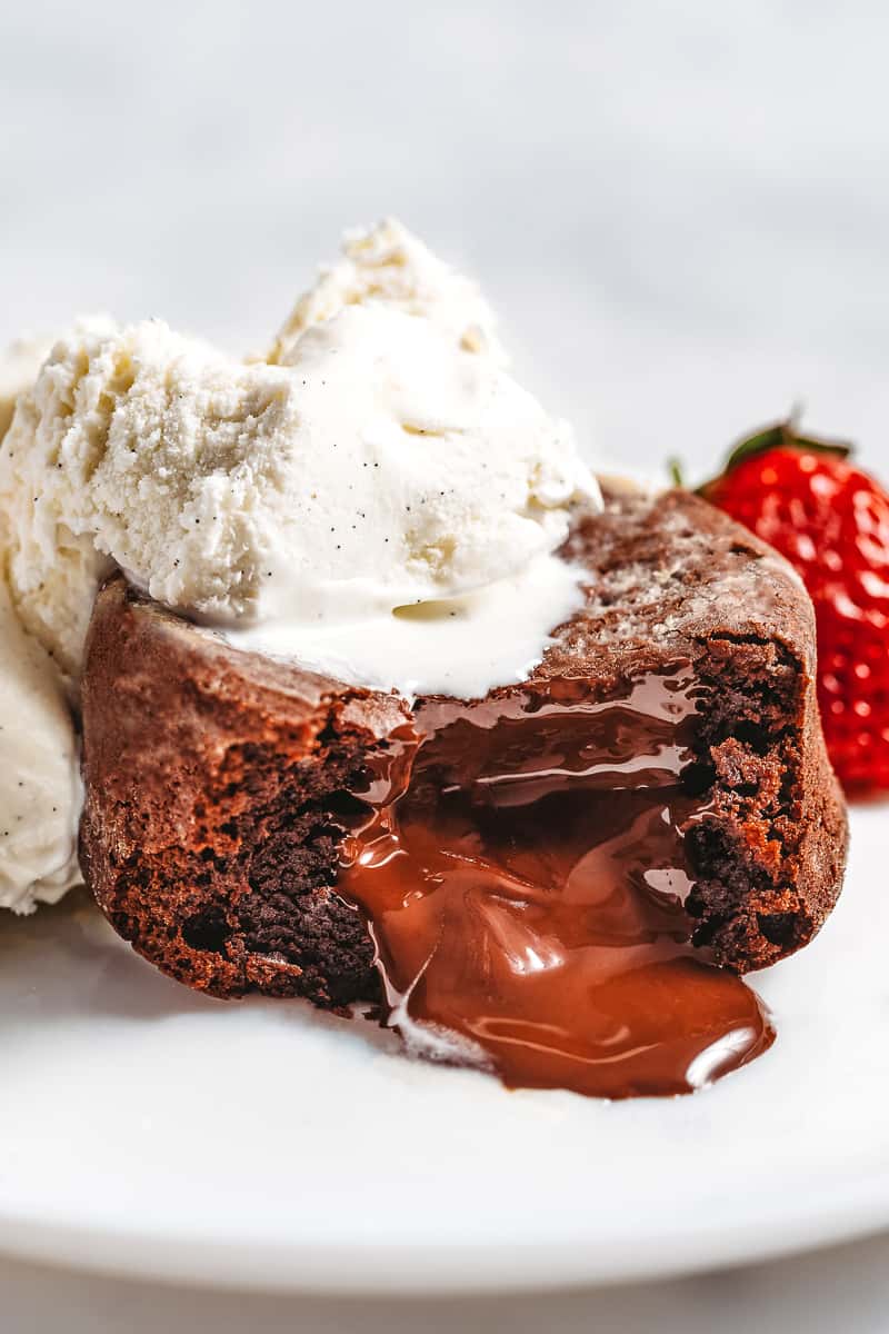 molten chocolate lave cake served on a plate topped with whipped cream and strawberries cut in half oozing