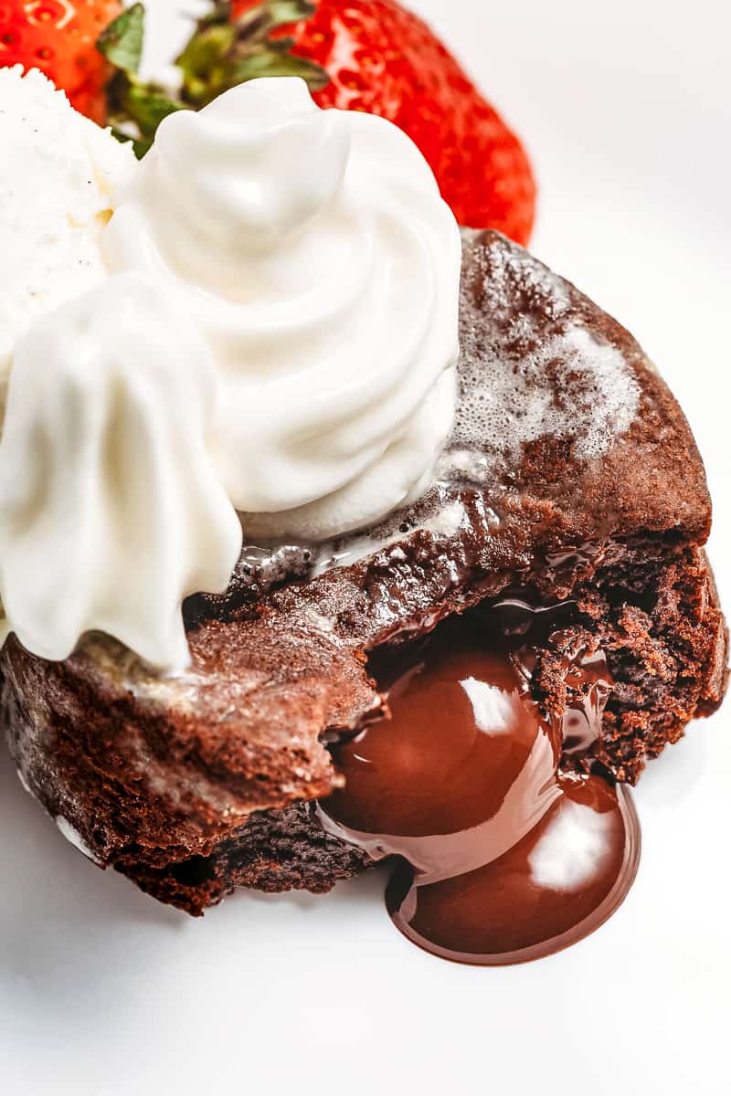 molten chocolate lava cake cut in half oozing out topped with whipped cream and strawberries served on a white plate