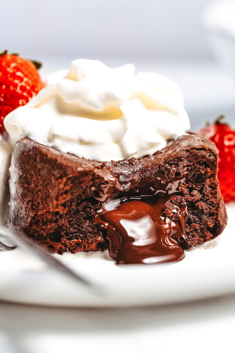 molten chocolate lava cake oozing served immediately on a white plate topped with whipped cream and strawberries cut in half
